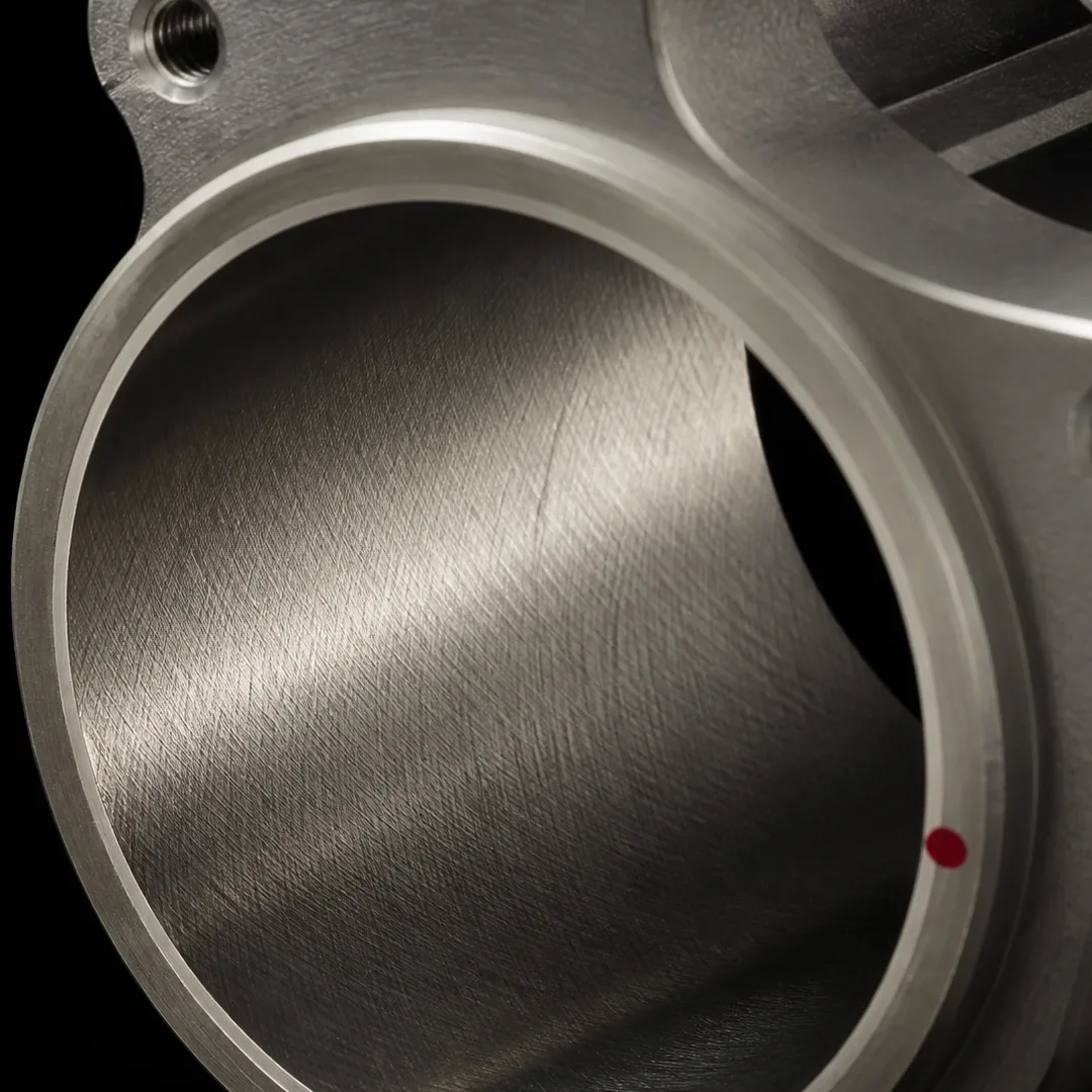 The inside wall of a honed bore in raking light, the cross-hatch running in two crossing directions across the full surface, a small red witness mark on the rim.
